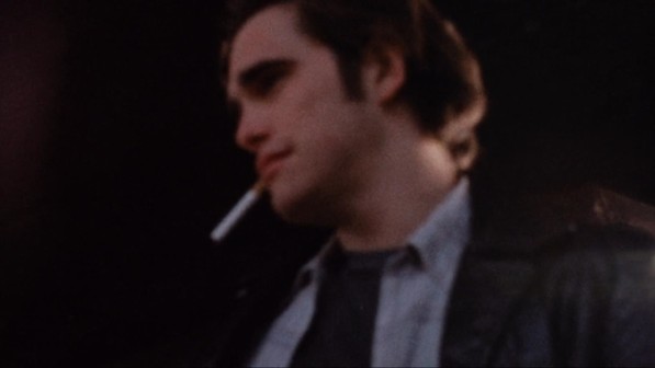 A slightly out of focus straight-on color medium close-up of Matt Dillon in profile, looking toward the left side of the frame, a cigarette dangling from his mouth