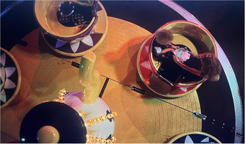 An extreme high-angle color long shot of two figures in a teacup ride at an amusement park